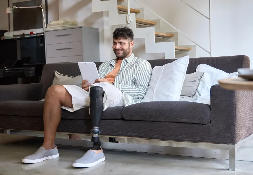 Young man with a prosthetic leg sitting on the lounge using an electronic tablet