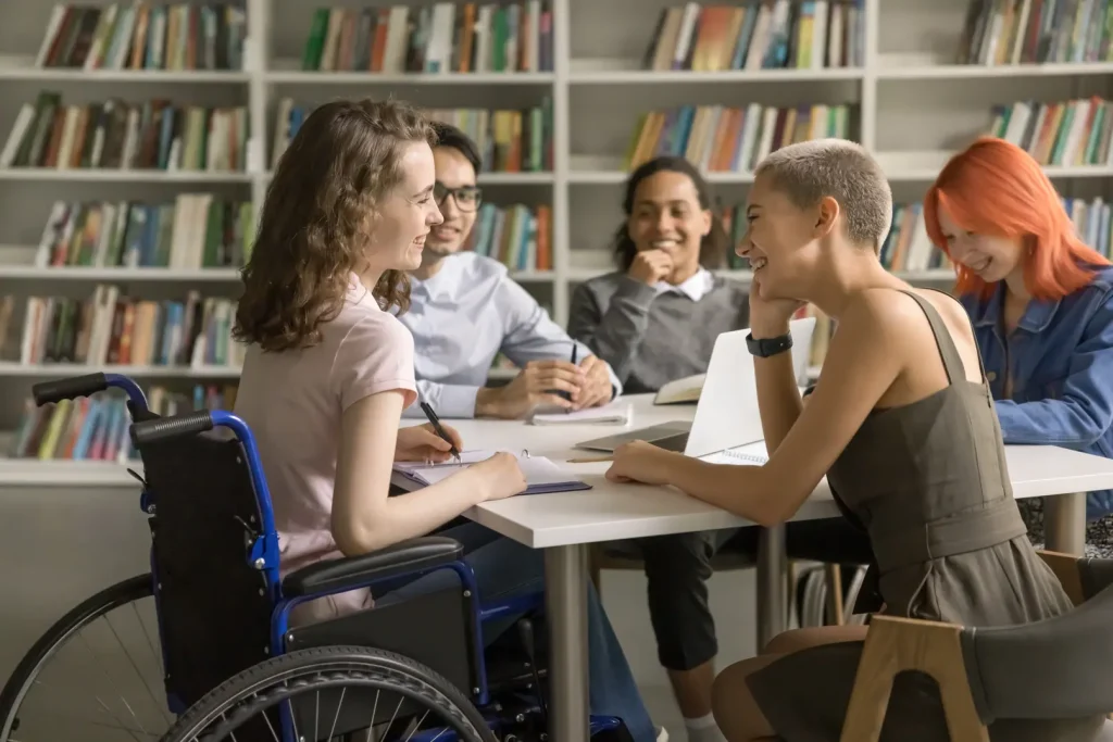 Young woman in wheelchair in a library setting sharing a conversation with her friends