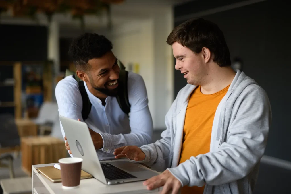 Man with disability smiling while using a computer with his male support worker to find a service through Minto Care
