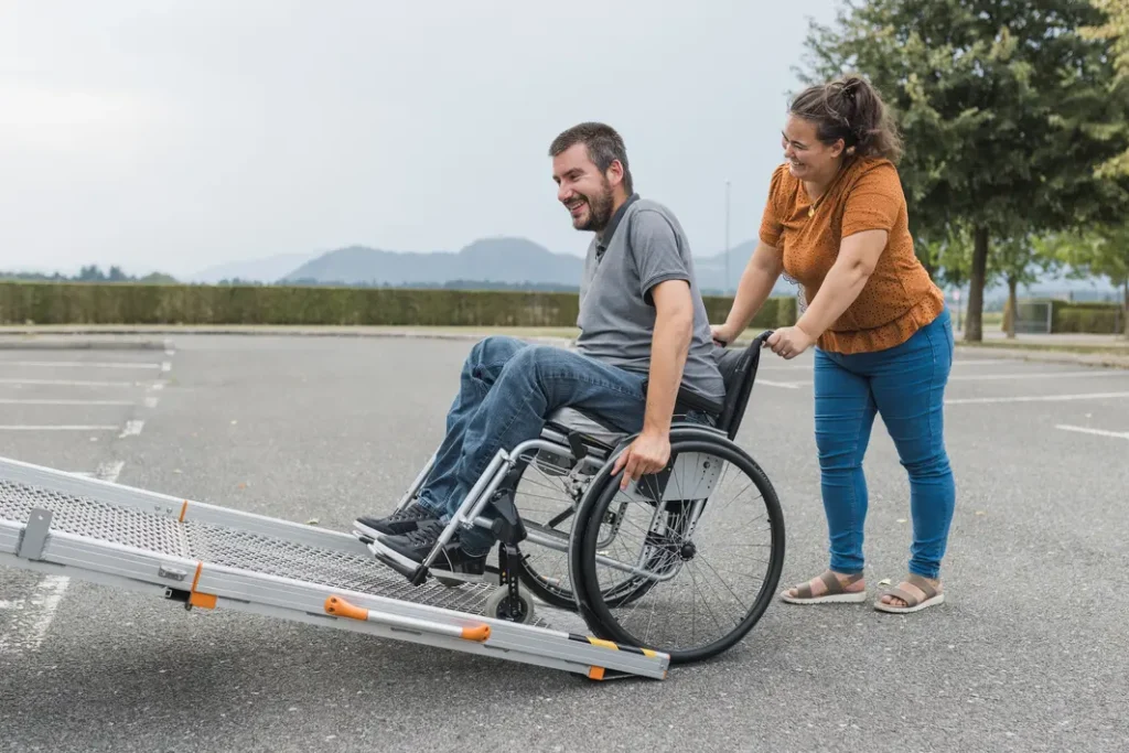 Man in wheelchair being assisted up a ramp into a car by his support worker